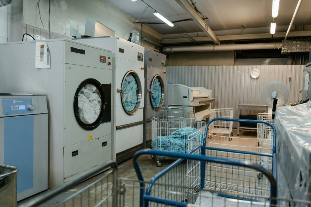 pexels photo 8774643 8774643 Interior view of an industrial laundry room with washers and rolling carts.