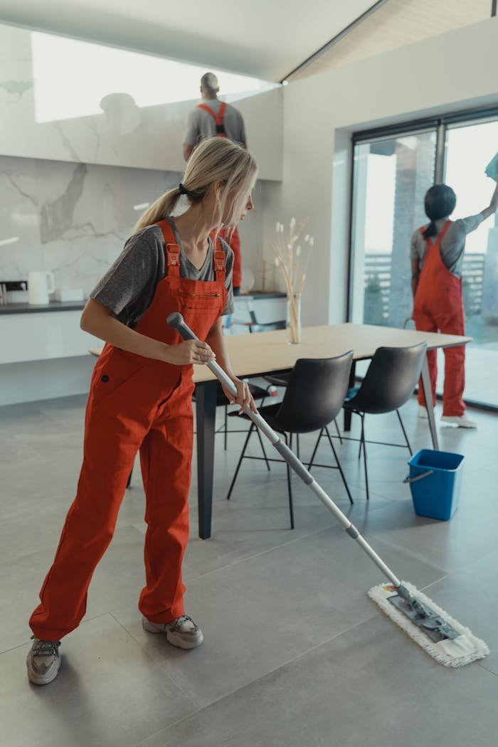 Home Cleaning team in red overalls mopping and sanitizing a modern home interior.