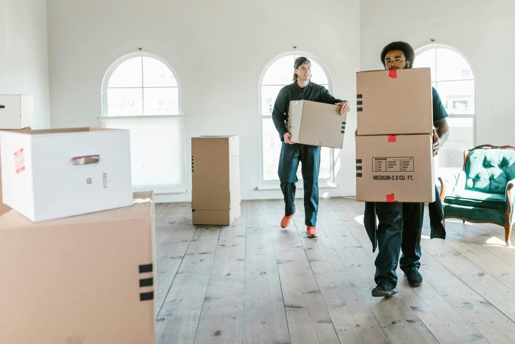 pexels photo 7464232 7464232 Two movers carrying boxes in a sunlit room, ready to assist with relocation.